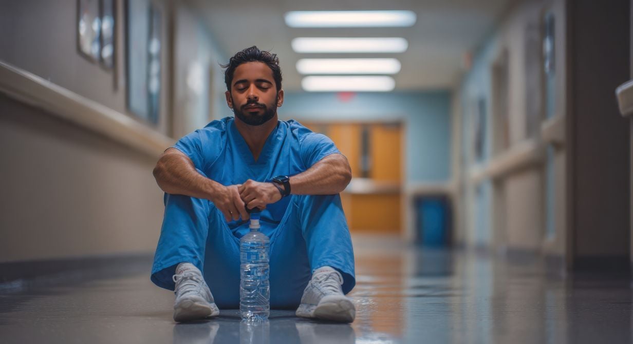 Exhausted healthcare worker sitting on a hospital floor, illustrating burnout and the ongoing healthcare staffing shortage in U.S. hospitals