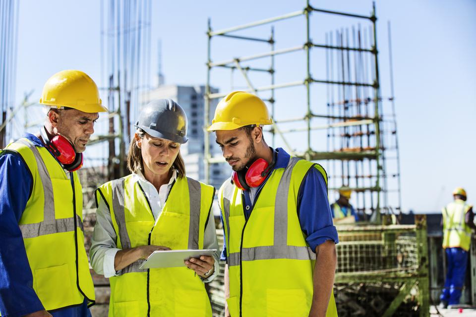 Three construction workers, working together on a tablet. 